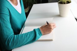 Woman in aqua sweater writing in a book
