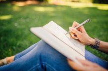 Hands of a woman writing in a notebook in a grassy field