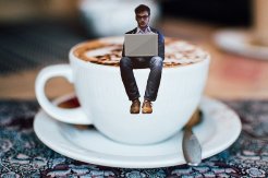 man sitting on the edge of a cup of coffee, writing on a laptop computer