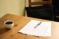 Wooden table with sheets of paper with a red pen on top and a cup of coffee on the side
