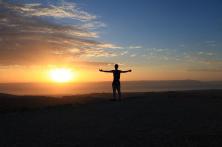 Silhouette of a person with arms outstretched looking at a sunrise