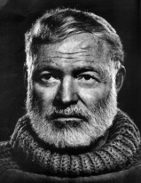 Black and white image of Ernest Hemingway's head with mustache and beard wearing a rugged turtleneck sweater