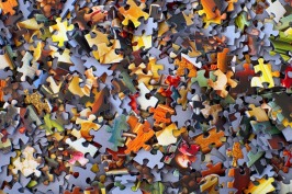 large number of small jigsaw puzzle pieces in blue, orange, yellow, green, and brown piled on top of each other