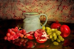 Still life with a grey/green pitcher, red and green grapes and red pomegranates