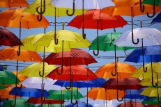 Fanciful painting of many red, orange yellow, blue, and green, and white open umbrellas floating in the sky