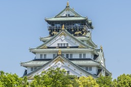 White and grey Japanese pagoda style building with blue sky and green treetops