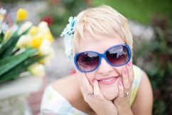 Smiling, happy-looking young woman with short blond hair and sunglasses with yellow and white tulips