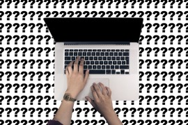 Hands typing on a laptop with a background of question marks